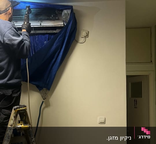 טכנאי מתקין מזגן על סולם בחדר